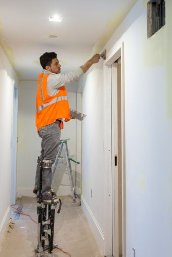 A worker plastering walls in the hallway while standing on stilts. Photo: Melissa Goodwin/For Commercial Observer