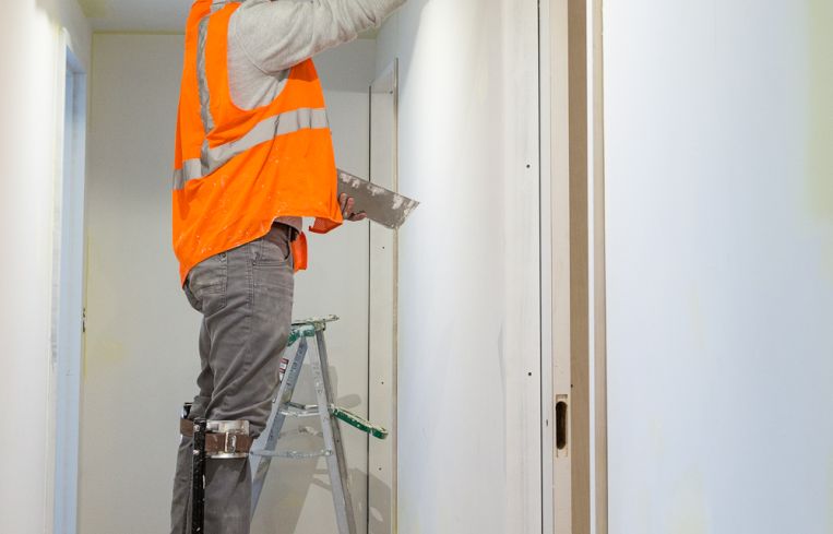A worker plastering walls in the hallway while standing on stilts. Photo: Melissa Goodwin/For Commercial Observer