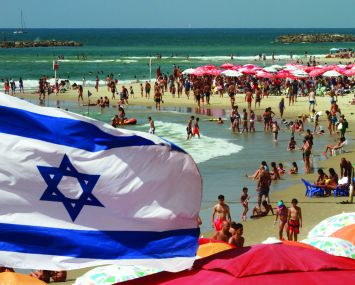 An Israeli flag flutters above umbrellas on the beaches of Tel Aviv. Photo: AFP/GIL COHEN-MAGEN