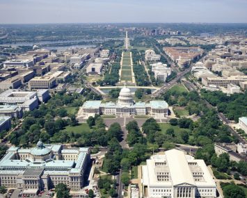 An aerial view of the domed Capitol Building with a long green space behind it.