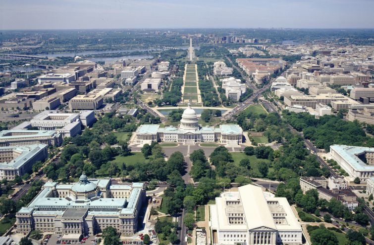 An aerial view of the domed Capitol Building with a long green space behind it.