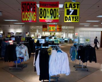A store with racks of clothing and there are going out of business signs above the racks.