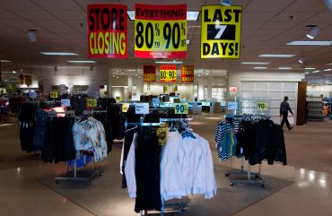 A store with racks of clothing and there are going out of business signs above the racks.