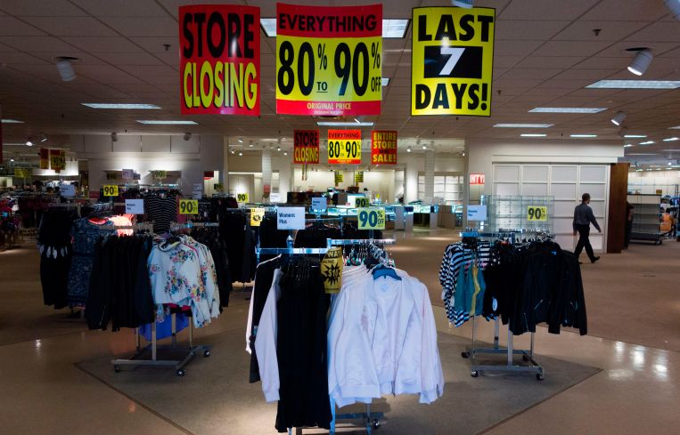 A store with racks of clothing and there are going out of business signs above the racks.