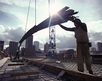 A crane lowers girders down to two workers on a construction site.