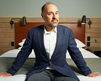 Mark Gordon sits on a bed at the Moxy Downtown, a millennial-focused hotel he recently developed in the Financial District.