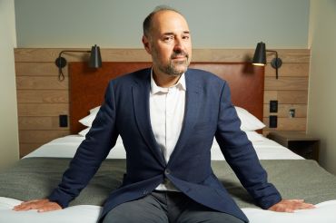 Mark Gordon sits on a bed at the Moxy Downtown, a millennial-focused hotel he recently developed in the Financial District.