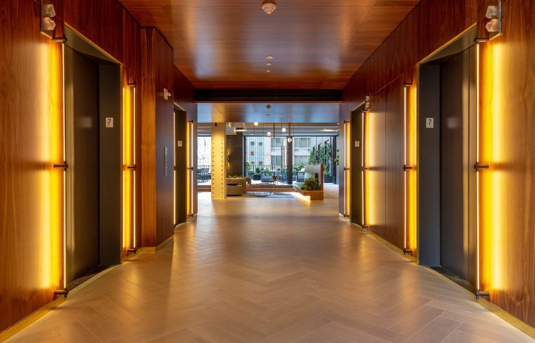 The elevator bank, clad in rich wood and long brushed brass lighting fixtures, opens to the lounge area and terrace.