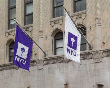 Purple and white NYU flags hang from a New York University building on West 4th Street in Manhattan.