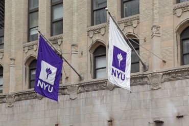 Purple and white NYU flags hang from a New York University building on West 4th Street in Manhattan. 
