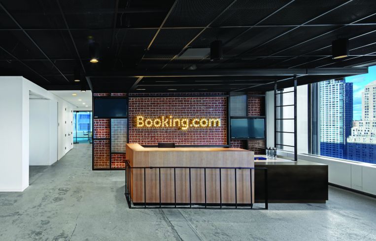 Booking.com's reception area has a lit up sign and a wood desk.