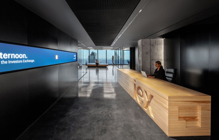 IEX's entryway is dark and features a natural wood reception desk and a long screen that displays market data and news.