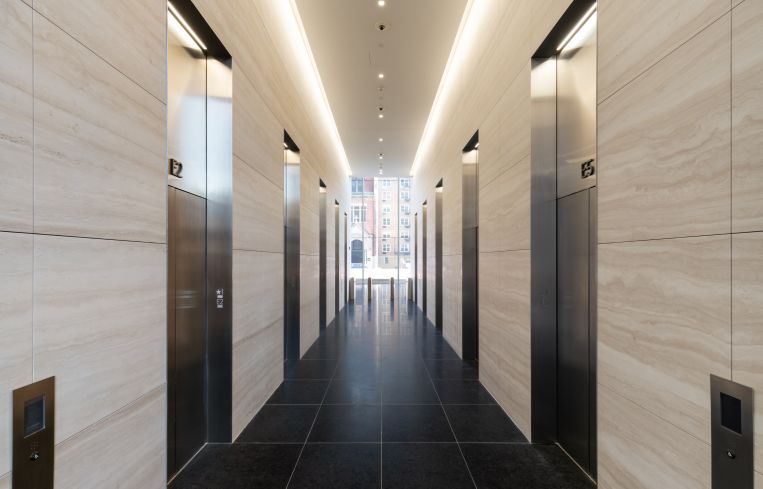 The white marble continues into the elevator lobby, which has bright overhead lighting and stainless steel elevator cabs.