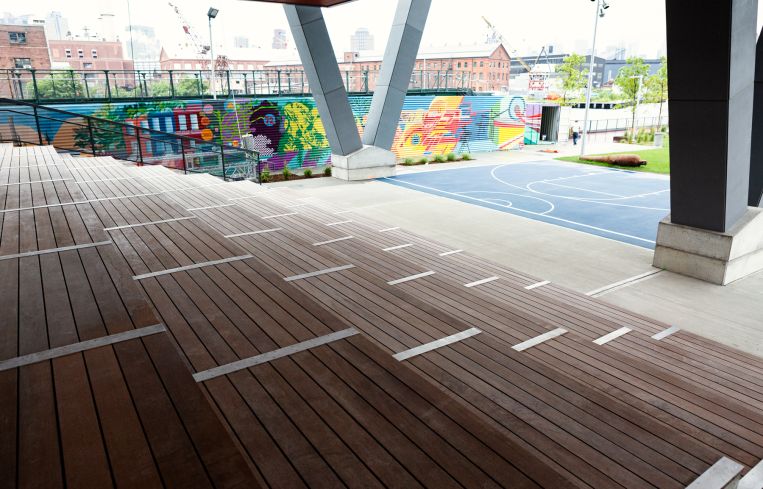 The outdoor space includes a large wooden seating area, a half-court basketball court and a lawn.