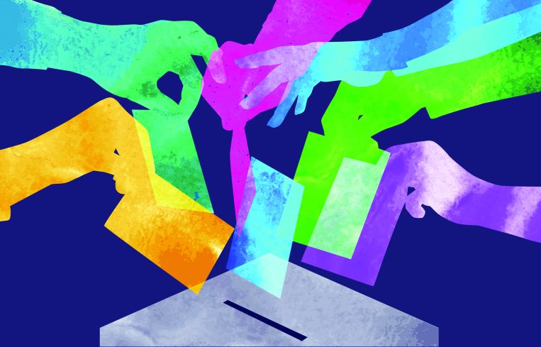 Several hands in several different colors casting a ballot.