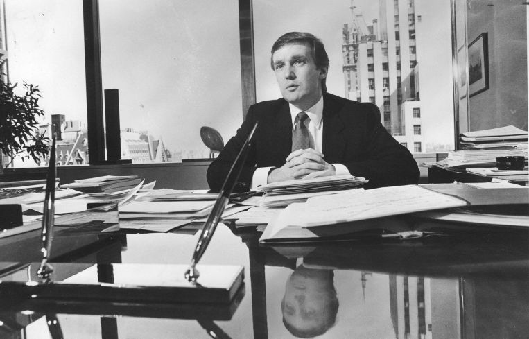 A man with his hands folded at the end of a long desk.