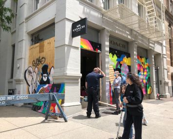 A police officer and onlookers surround the looted Coach store on Prince Street at West Broadway.