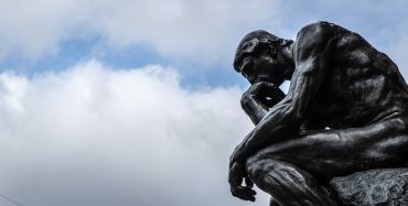 The sculpture "The Thinker" ("Le Penseur") by the sculptor Auguste Rodin can be seen against a cloudy sky.