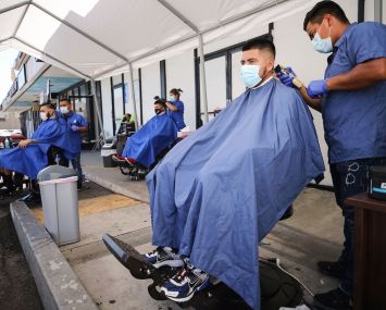 Barbers from King's Cutz in L.A. give haircuts beneath an awning outside. This week, barbershops and hair salons in L.A. can move operations indoors at 25-percent capacity, but they are encouraged to operate outdoors as much as possible to prevent the spread of coronavirus.