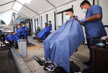 Barbers from King's Cutz in L.A. give haircuts beneath an awning outside. This week, barbershops and hair salons in L.A. can move operations indoors at 25-percent capacity, but they are encouraged to operate outdoors as much as possible to prevent the spread of coronavirus.