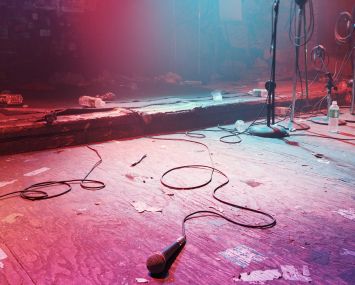 An empty, darkened stage with just a mic lying on top of it.