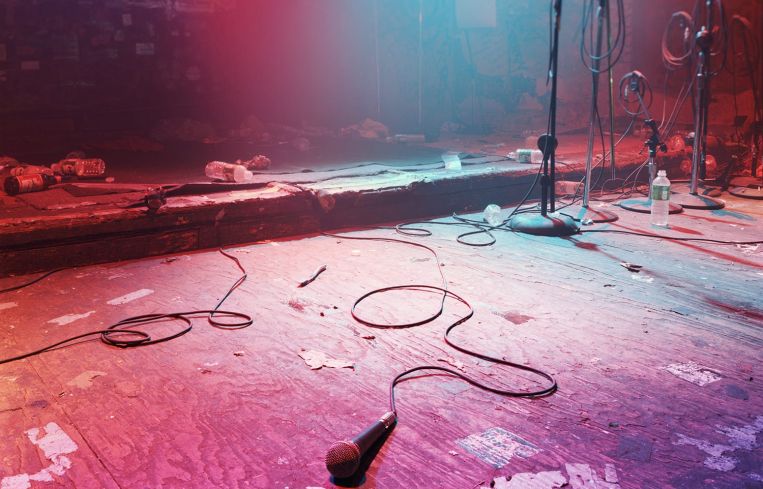 An empty, darkened stage with just a mic lying on top of it.