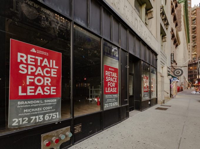 Empty storefronts with leasing signs on them along an empty sidewalk.