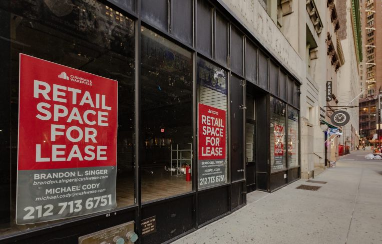 Empty storefronts with leasing signs on them along an empty sidewalk.