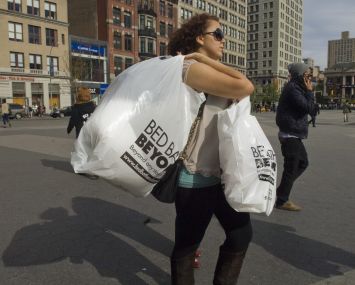 A woman carrying full plastic bags across a street.