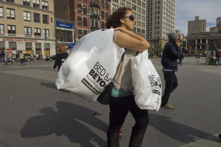 A woman carrying full plastic bags across a street.