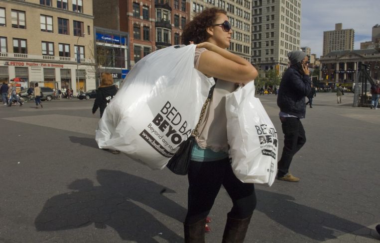 A woman carrying full plastic bags across a street.