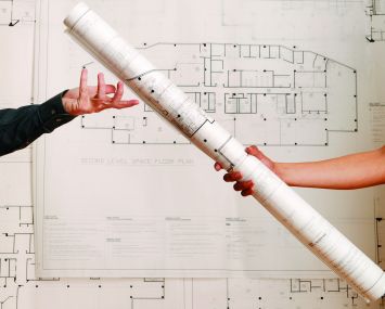 One arm handing off a rolled-up blueprint to another arm.