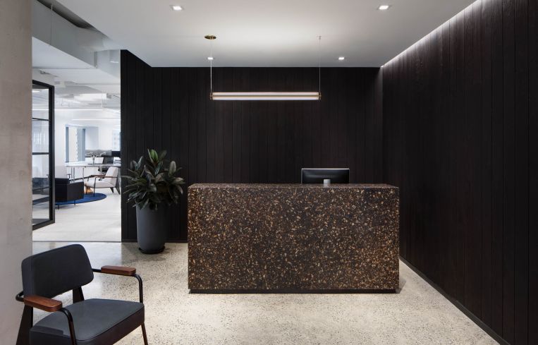The reception area features blackened wood walls and a wood terrazzo desk.