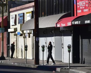 A man speaks on his cellphone in front of a row of shuttered small businesses in Los Angeles.