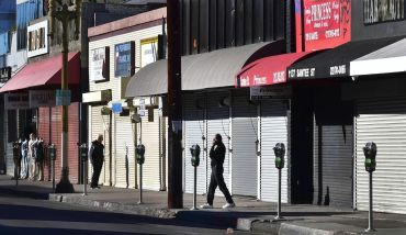 A man speaks on his cellphone in front of a row of shuttered small businesses in Los Angeles.