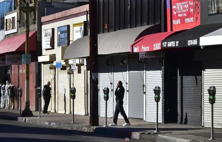 A man speaks on his cellphone in front of a row of shuttered small businesses in Los Angeles.