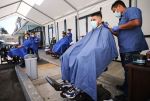 Barbers from King's Cutz in L.A. give haircuts beneath an awning outside. Barbershops and hair salons in L.A. were allowed to move operations indoors at 25-percent capacity, but that changed again amid the most recent coronavirus surge.