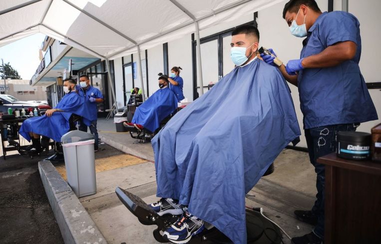 Barbers from King's Cutz in L.A. give haircuts beneath an awning outside. Barbershops and hair salons in L.A. were allowed to move operations indoors at 25-percent capacity, but that changed again amid the most recent coronavirus surge.