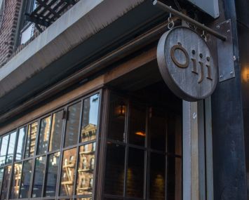 The outside of a restaurant with an oval sign hanging outside.