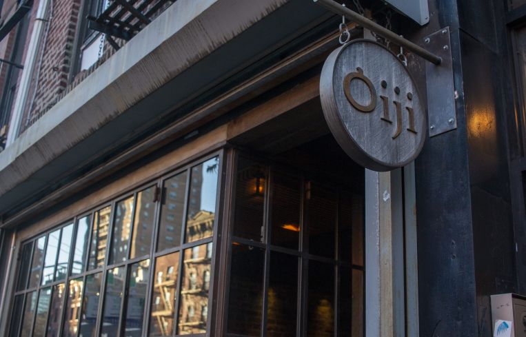 The outside of a restaurant with an oval sign hanging outside.