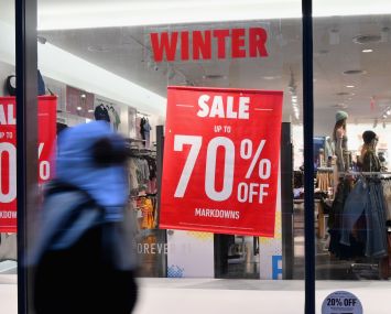 Someone in a rain jacket walks by a storefront with a "70 percent off" sign on it.