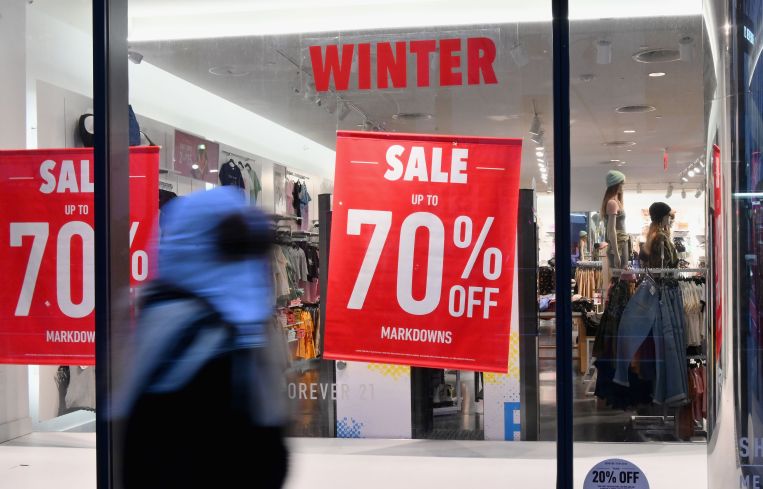 Someone in a rain jacket walks by a storefront with a "70 percent off" sign on it.