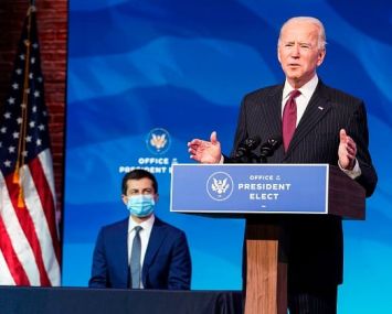 Two men, one standing at a podium and the other seated behind him.