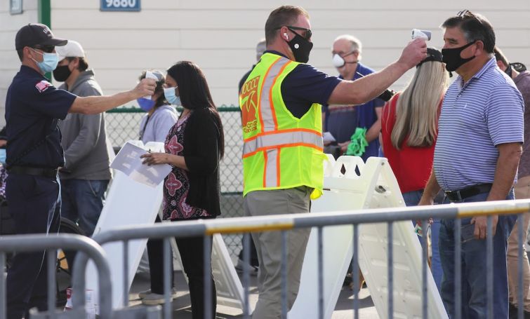 People receive temperature checks while waiting in line to receive the COVID-19 vaccine at a mass vaccination site in a parking lot for Disneyland Resort in January 2021 in