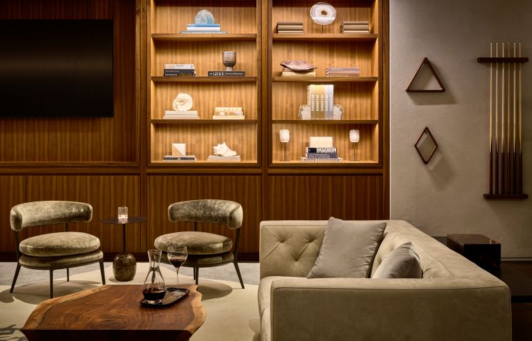 The "whiskey library" hosts shelving with nicknacks and books, along with gray and yellow midcentury couches and chairs and live edge coffee tables.