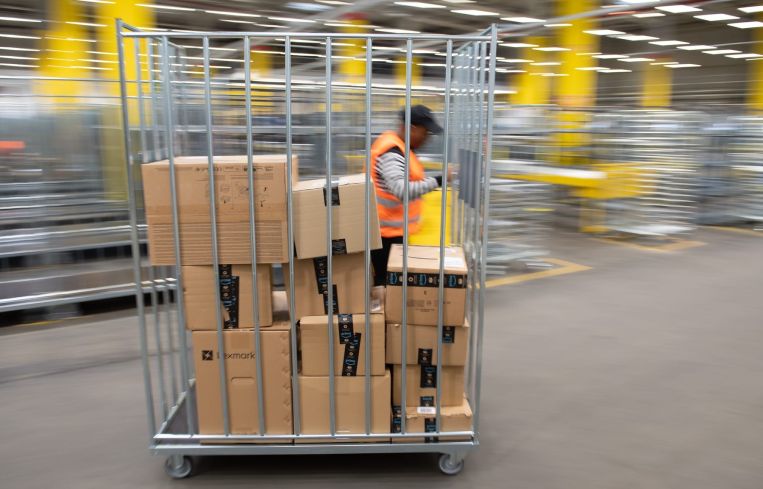 An Amazon sorting employee pulls a cart with parcels in a distribution center.