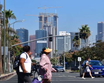 Pedestrians cross a street against a backdrop of luxury highrise apartments under construction in Los Angeles