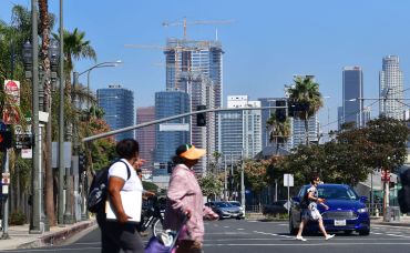 Pedestrians cross a street against a backdrop of luxury highrise apartments under construction in Los Angeles