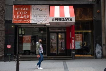 A person wearing a mask walks past a For Lease sign at a closed down TGI Fridays in the Financial District on October 22, 2020 in New York City.