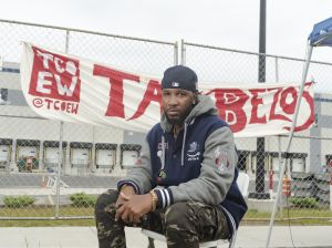 Chris Smalls sits in front of a sign reading "Tax Bezos." Smalls has been organizing for an independent Amazon Labor Union since he led a protest advocating for stronger coronavirus safety precautions at the company's Staten Island facility. 